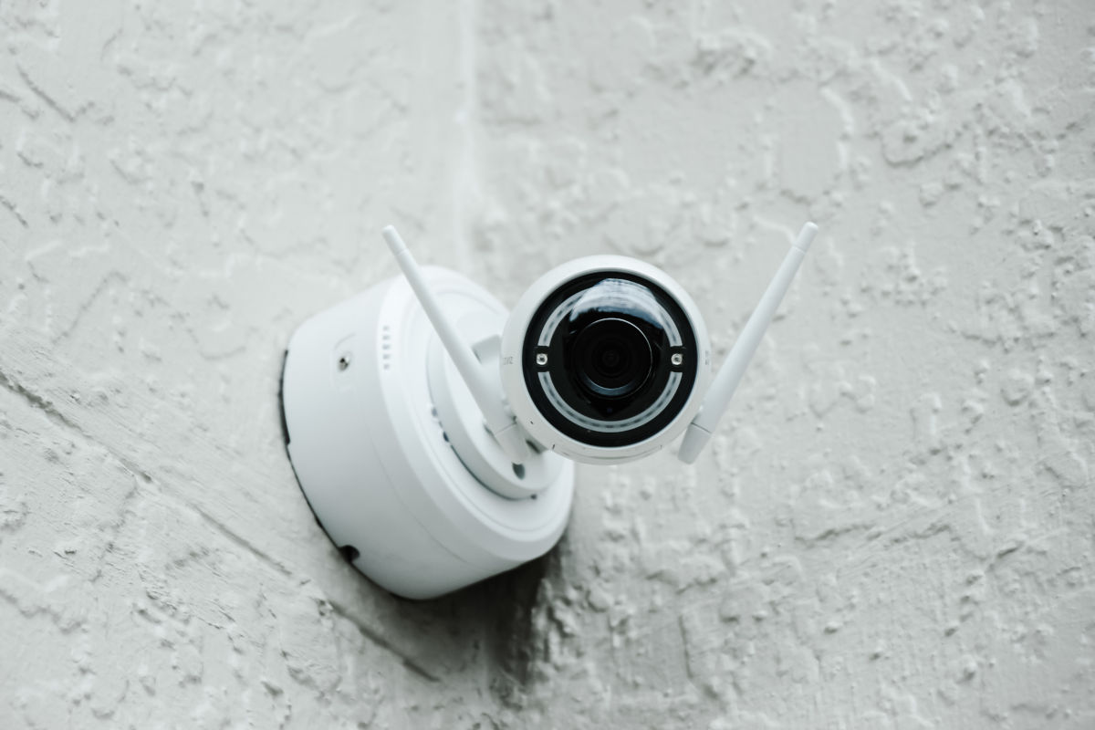 Camera de securitate alba montata pe un perete, cu iluminare nocturna pentru o supraveghere eficienta.