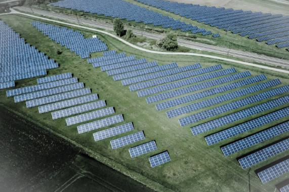 Vedere aeriana cu panouri fotovoltaice dispuse pe un camp, evidentiind utilizarea energiei solare.