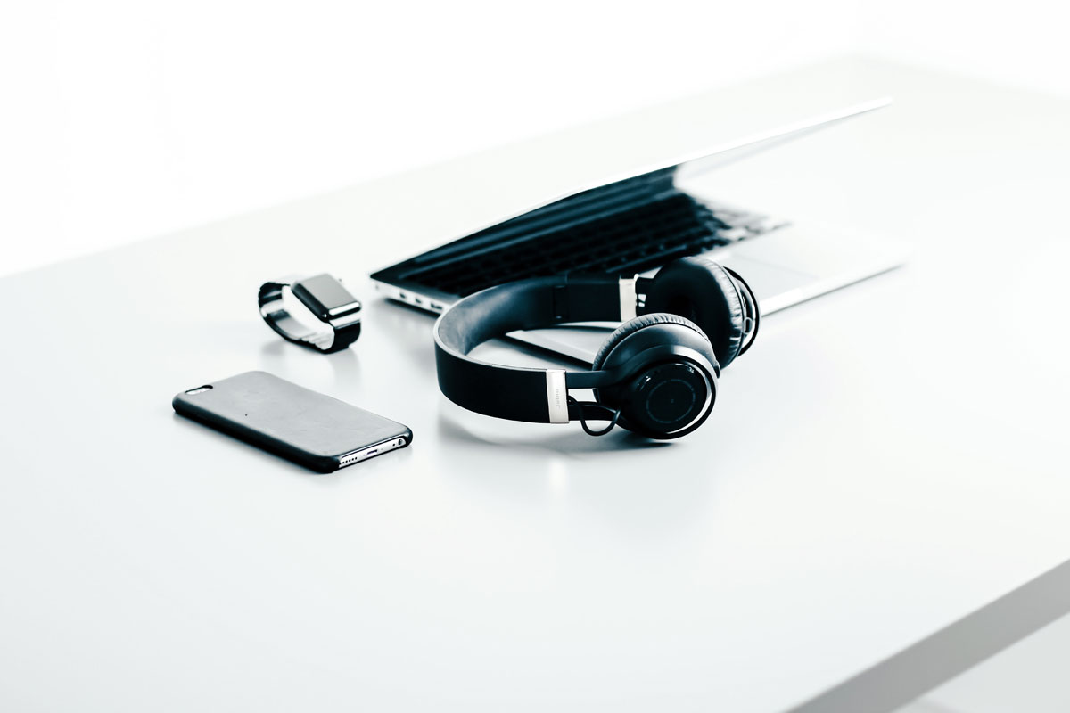 Un laptop, casti cablu audio, si un telefon mobil pe o masa alba, perfect pentru un birou minimalist si elegant.