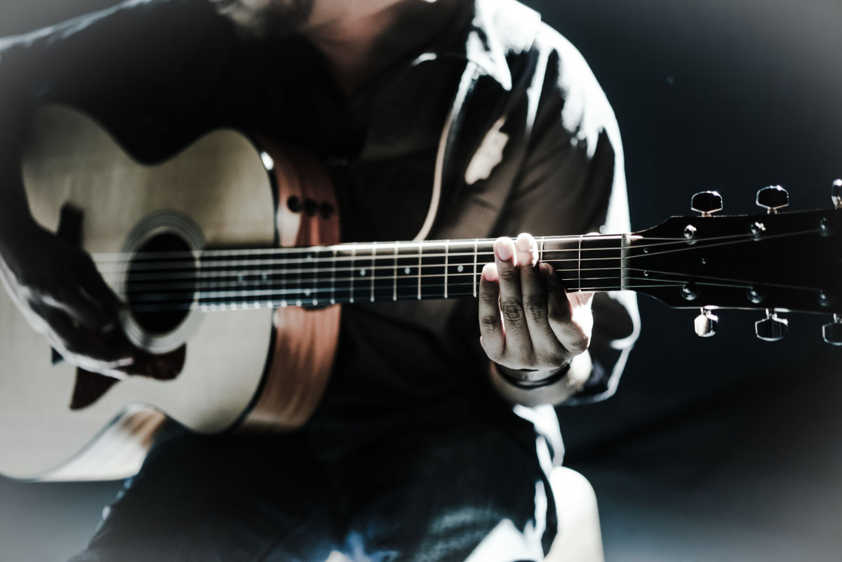 Barbatul se bucura de muzica, cantand la chitara acustica, cu boxa USB in fundal.