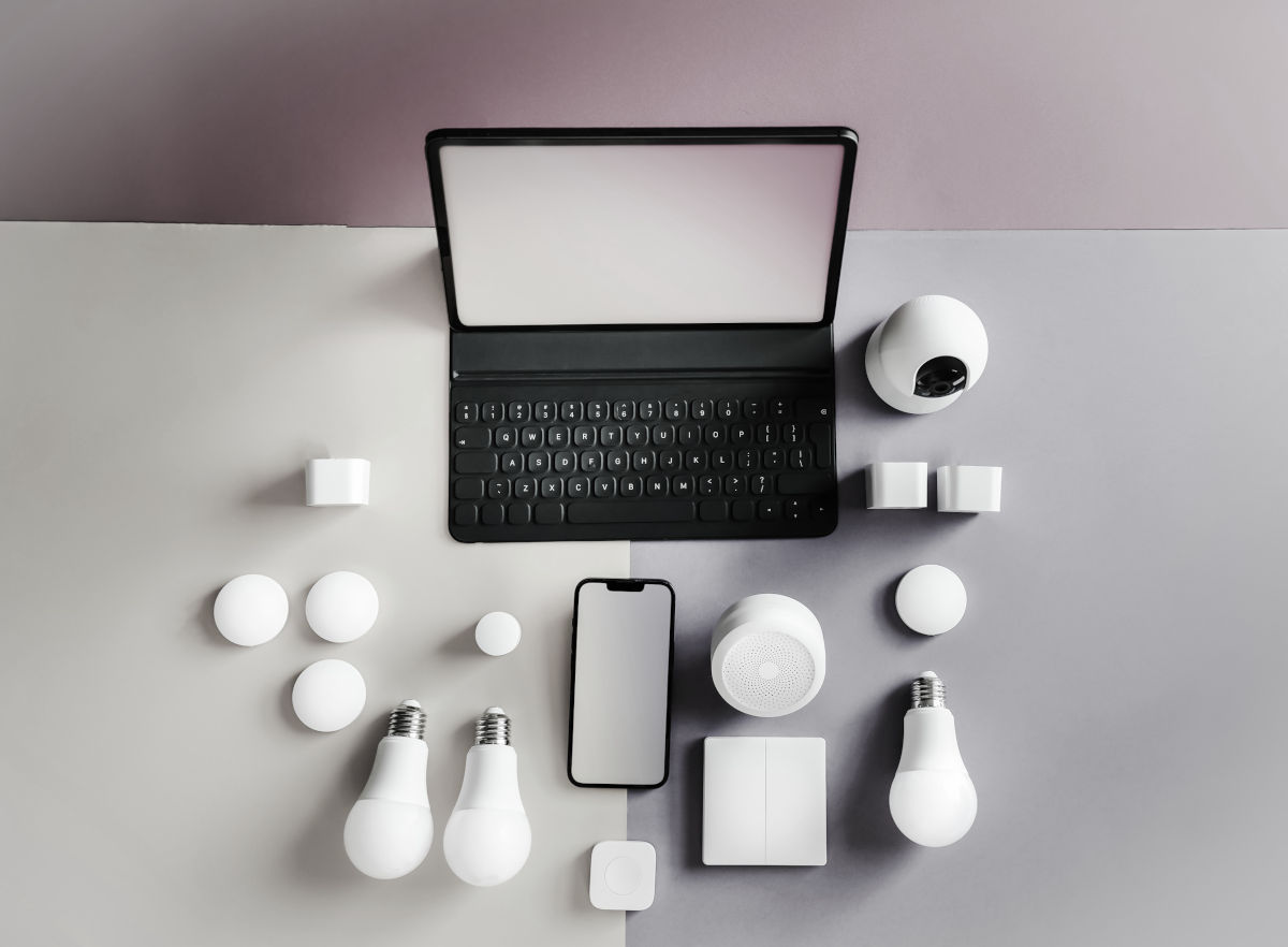 Laptop, telefon si alte dispozitive electronice pe o masa, cu un iluminator wireless in fundal.
