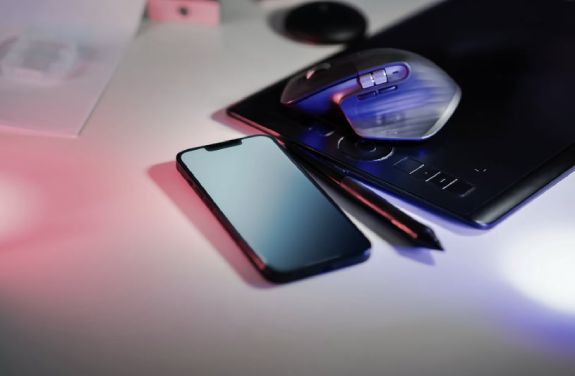 Pe un birou se afla un smartphone, un mouse si un stilou, evidentiind tehnologia, conectivitatea si creativitatea.