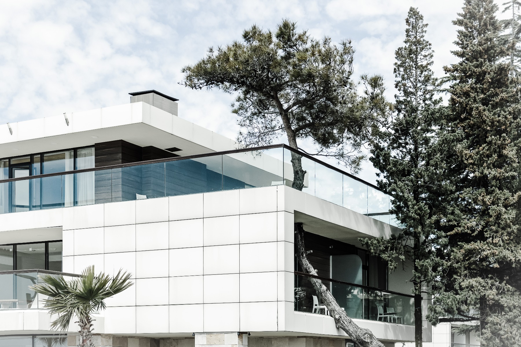 Casa moderna alba, cu balcon si copaci, evidențiind un stil de viața eco-friendly si armonie cu natura.