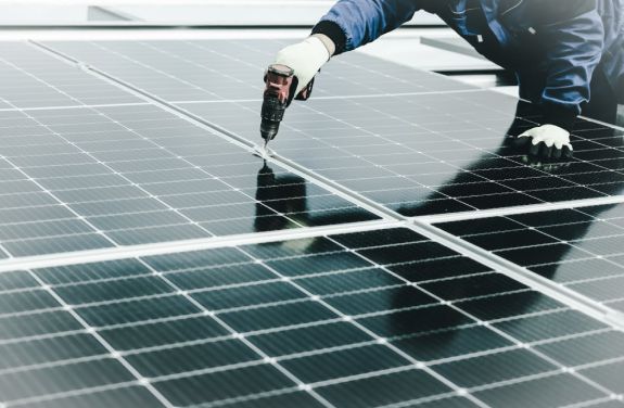 O persoana imbracata intr-o jacheta albastra si manusi, instaland un panouri solare cu microinvertor.