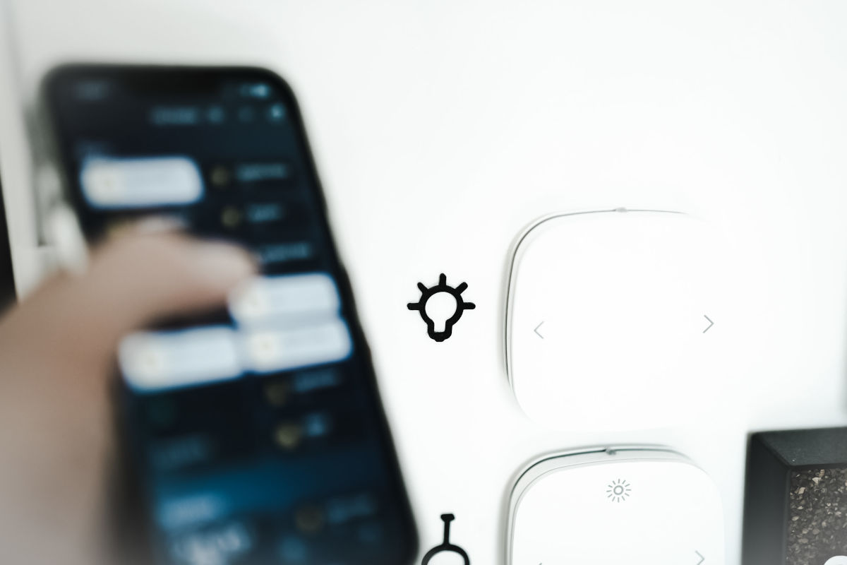 O persoana foloseste un smartphone pentru a controla un intrerupator de lumina, conectat la un punct de acces WiFi iar pe un perete se discerne un access point wifi.