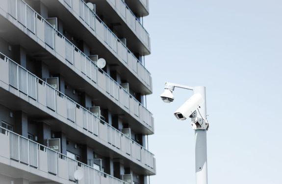 O camera de supraveghere amplasata la inaltime, in fata unei cladiri inalte, pentru monitorizarea eficienta a zonei.